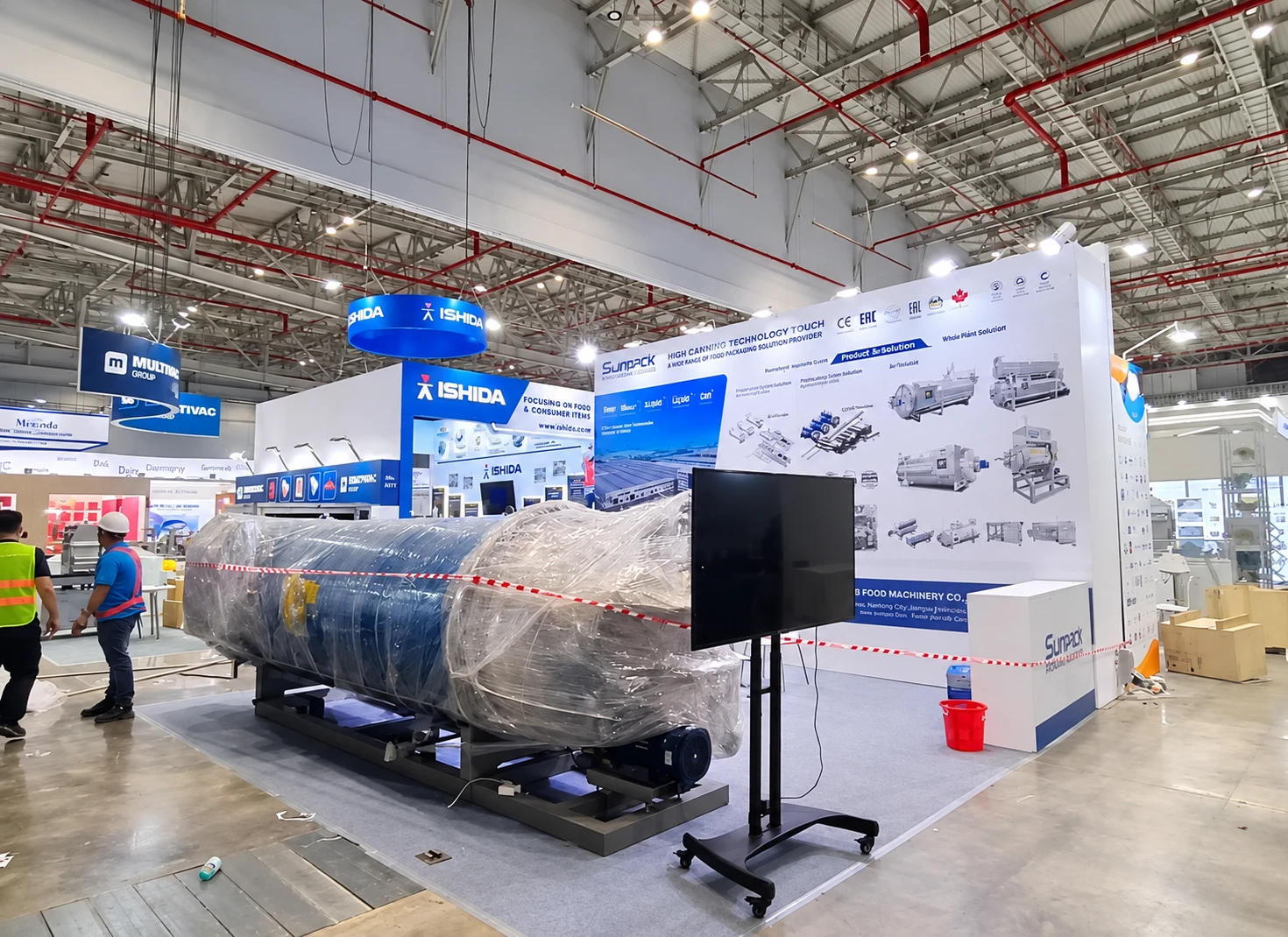 SUNPACK processing equipment exhibition space with a large cylindrical machine, technical backdrop and freestanding monitor