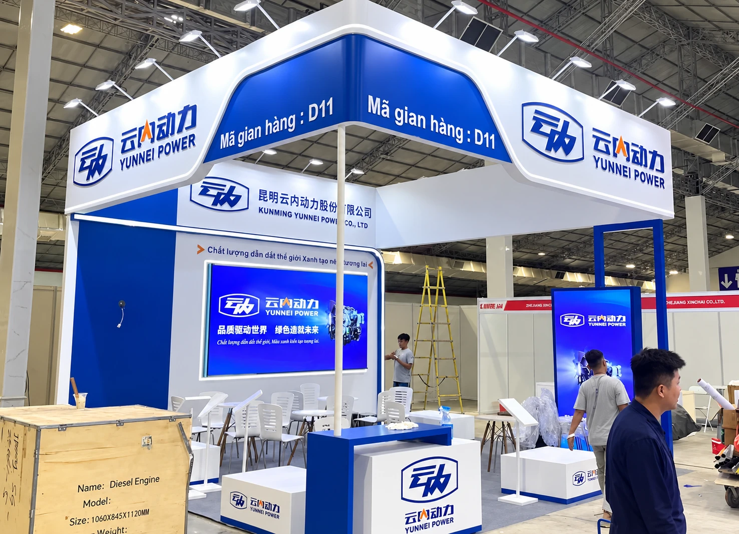 Blue and white YUNNEI POWER booth with overhead branding, open seating and product displays
